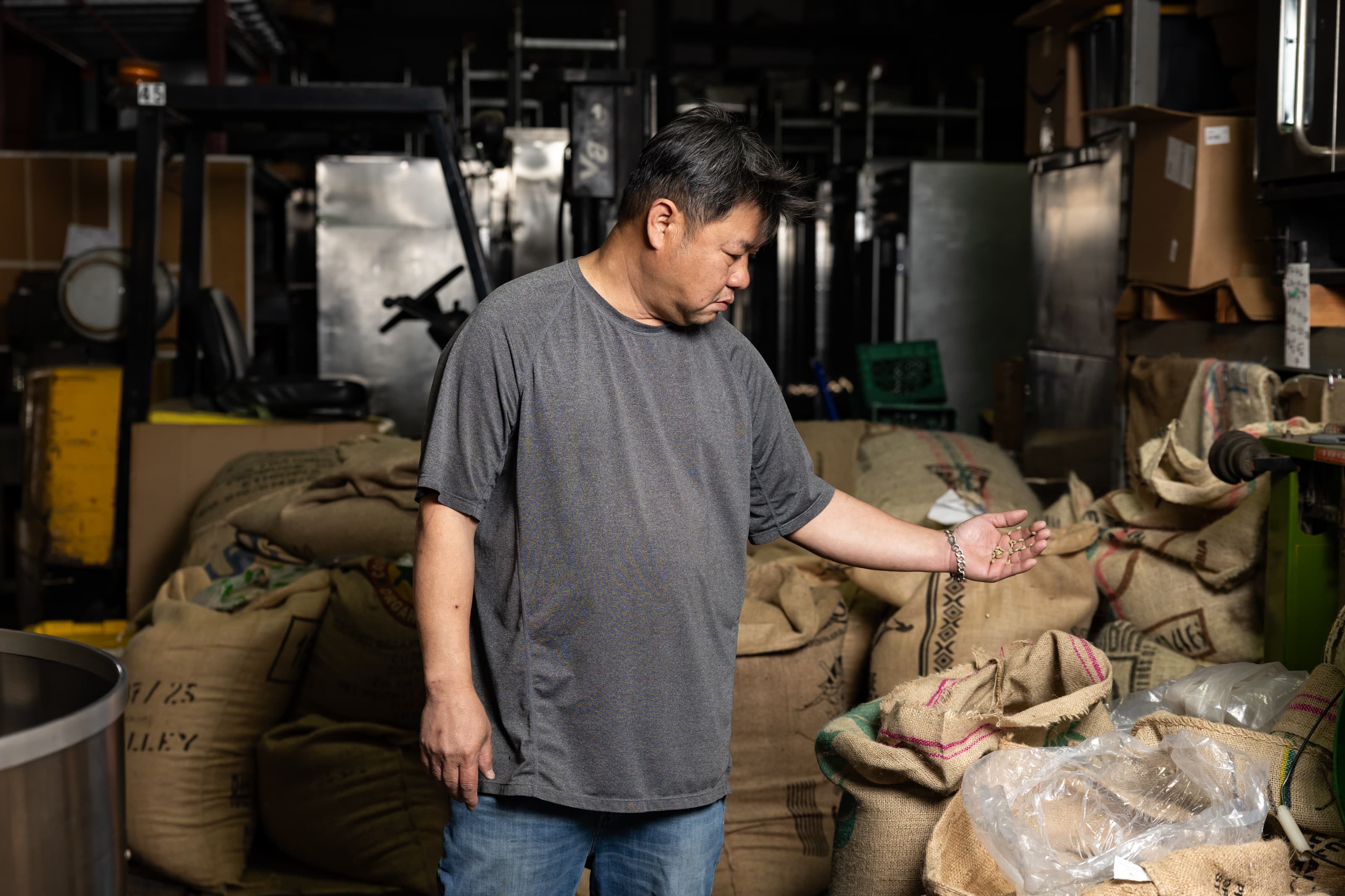 Van Ho examining a handful of green coffee beans in his palm inside the roastery.