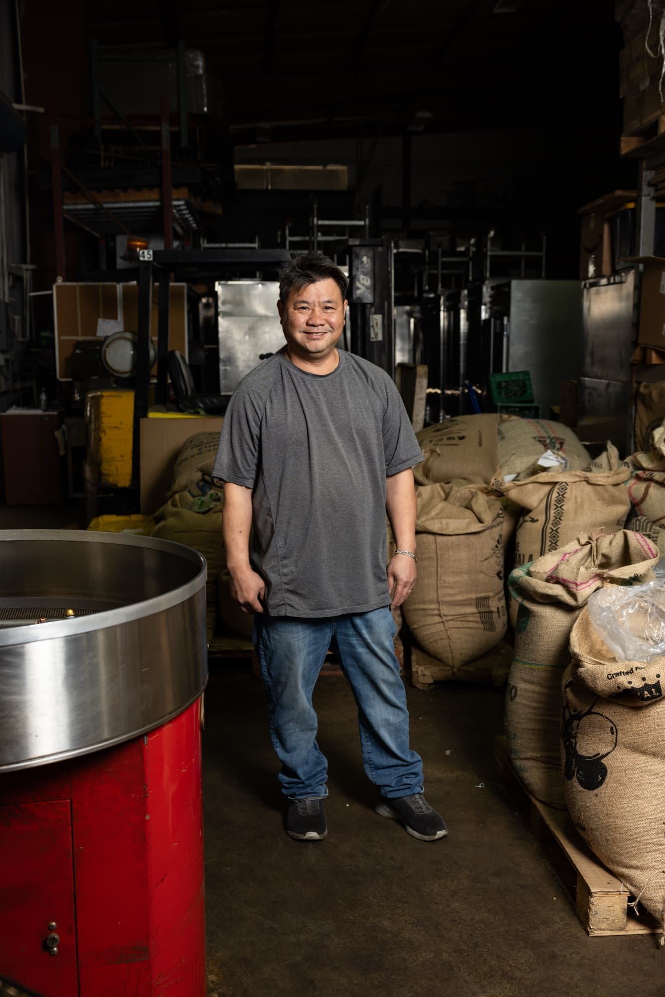 Van Ho, owner of Sam's Coffee Roasters, in the warehouse beside the roaster and coffee sacks.
